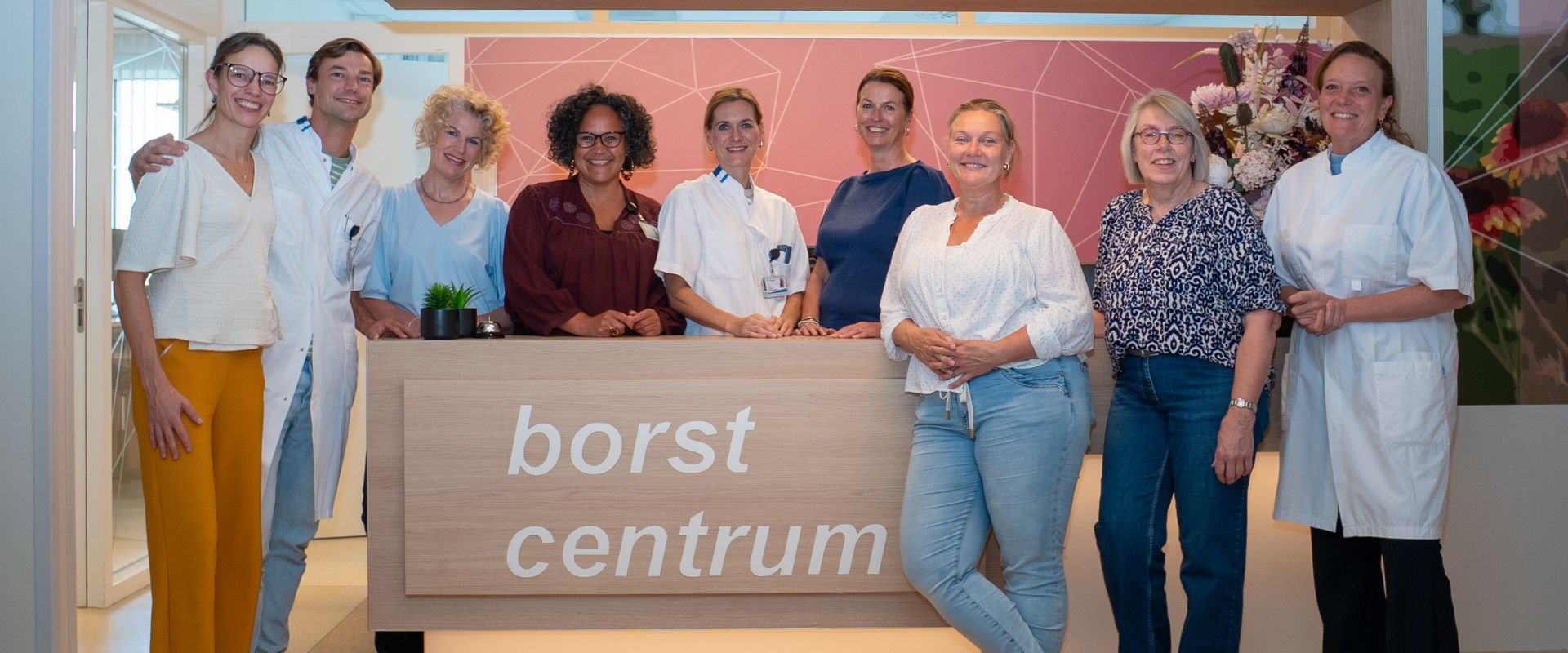 Groep mensen poseert voor het "Borstcentrum" bord in een medische omgeving.