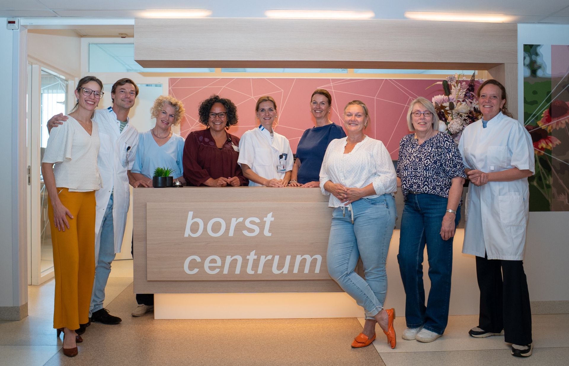 Groep mensen poseert voor het "Borstcentrum" bord in een medische omgeving.