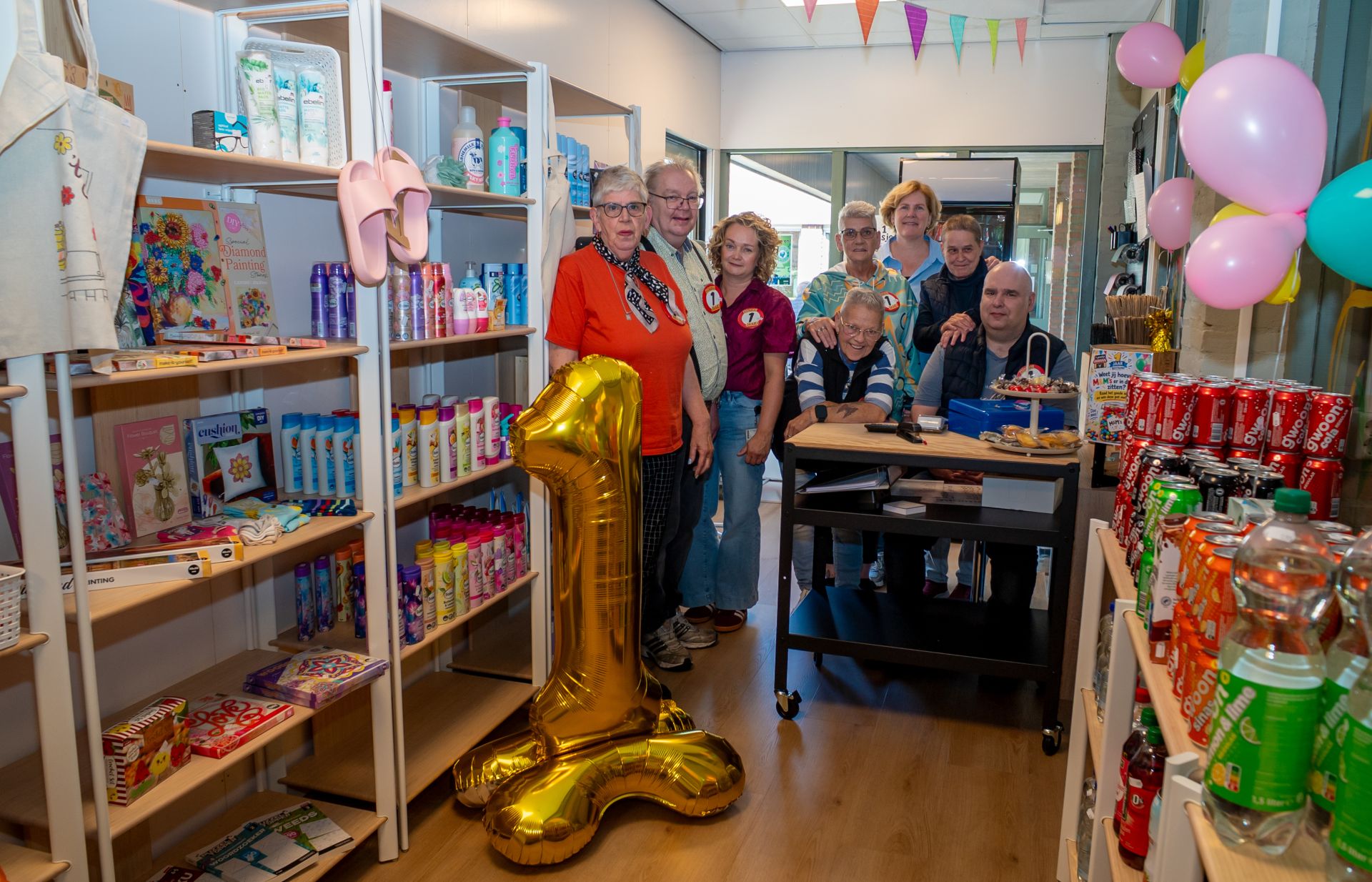 Een groep mensen viert de eerste verjaardag van een winkel met decoraties en feestelijke ballonnen.