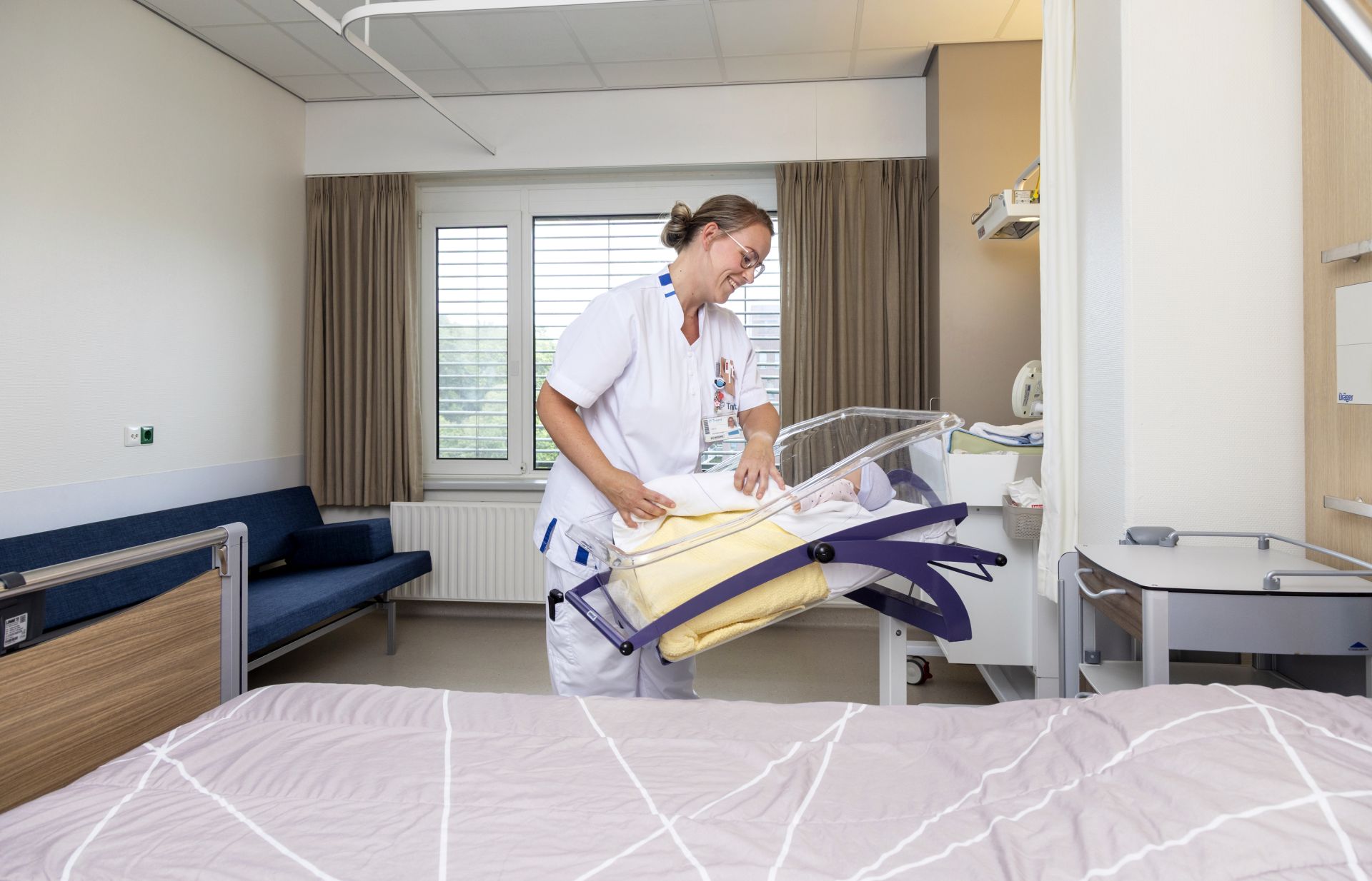 Zorgverlener maakt een ziekenhuisbed op in een heldere kamer.