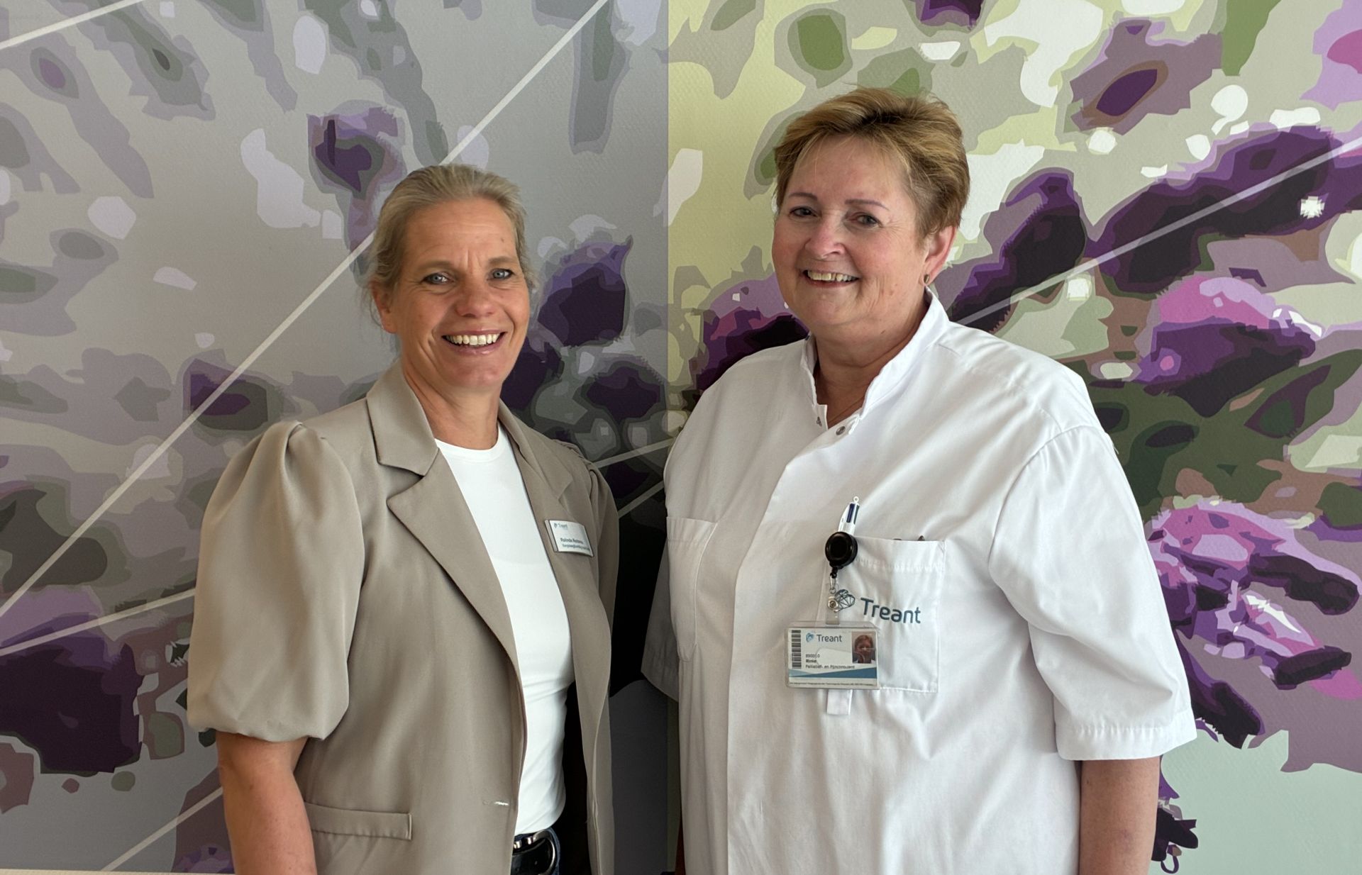 Twee vrouwen poseren samen voor een kleurrijke, abstracte achtergrond.