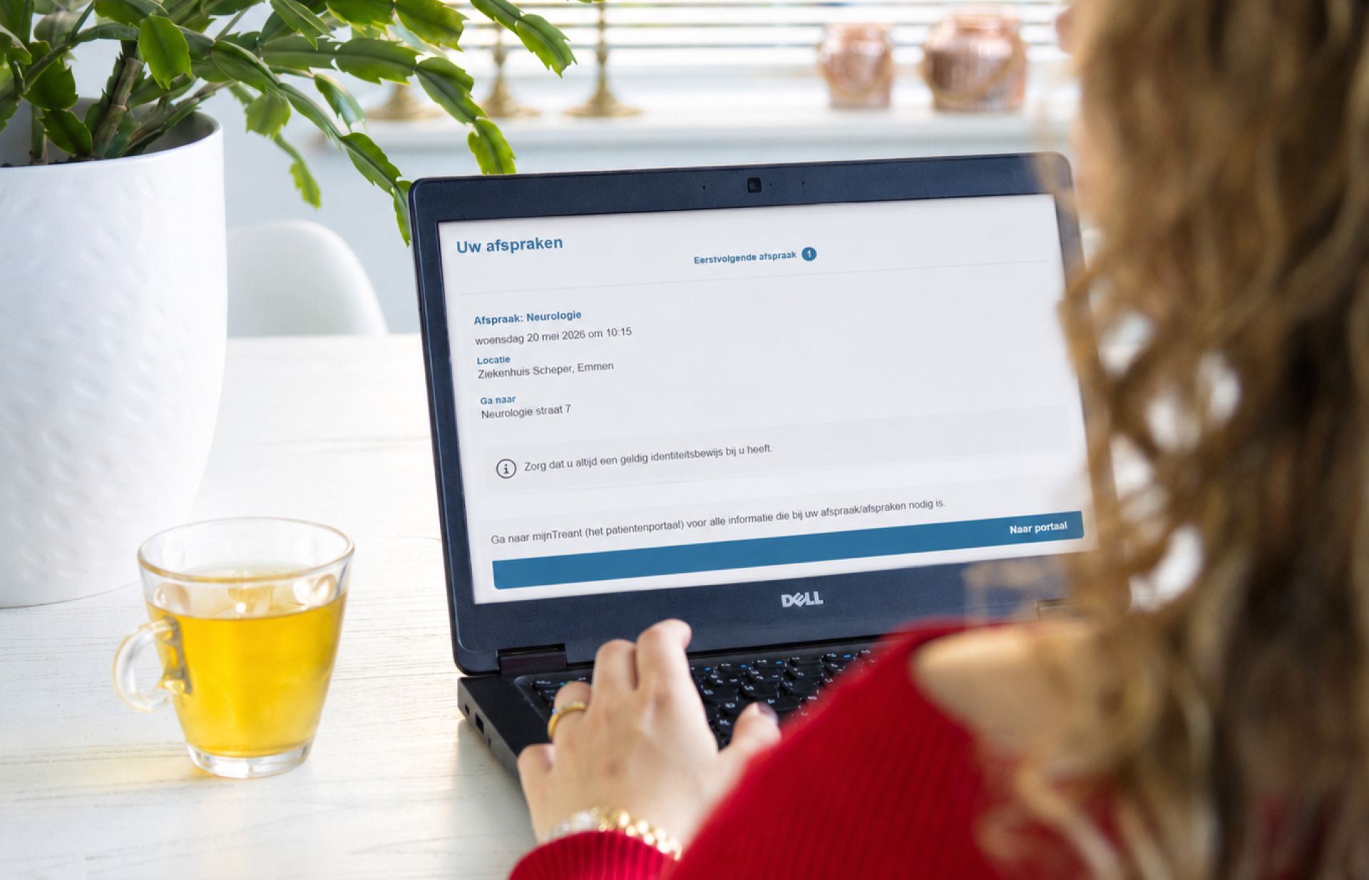 Een persoon werkt op een laptop met een kopje thee op tafel.