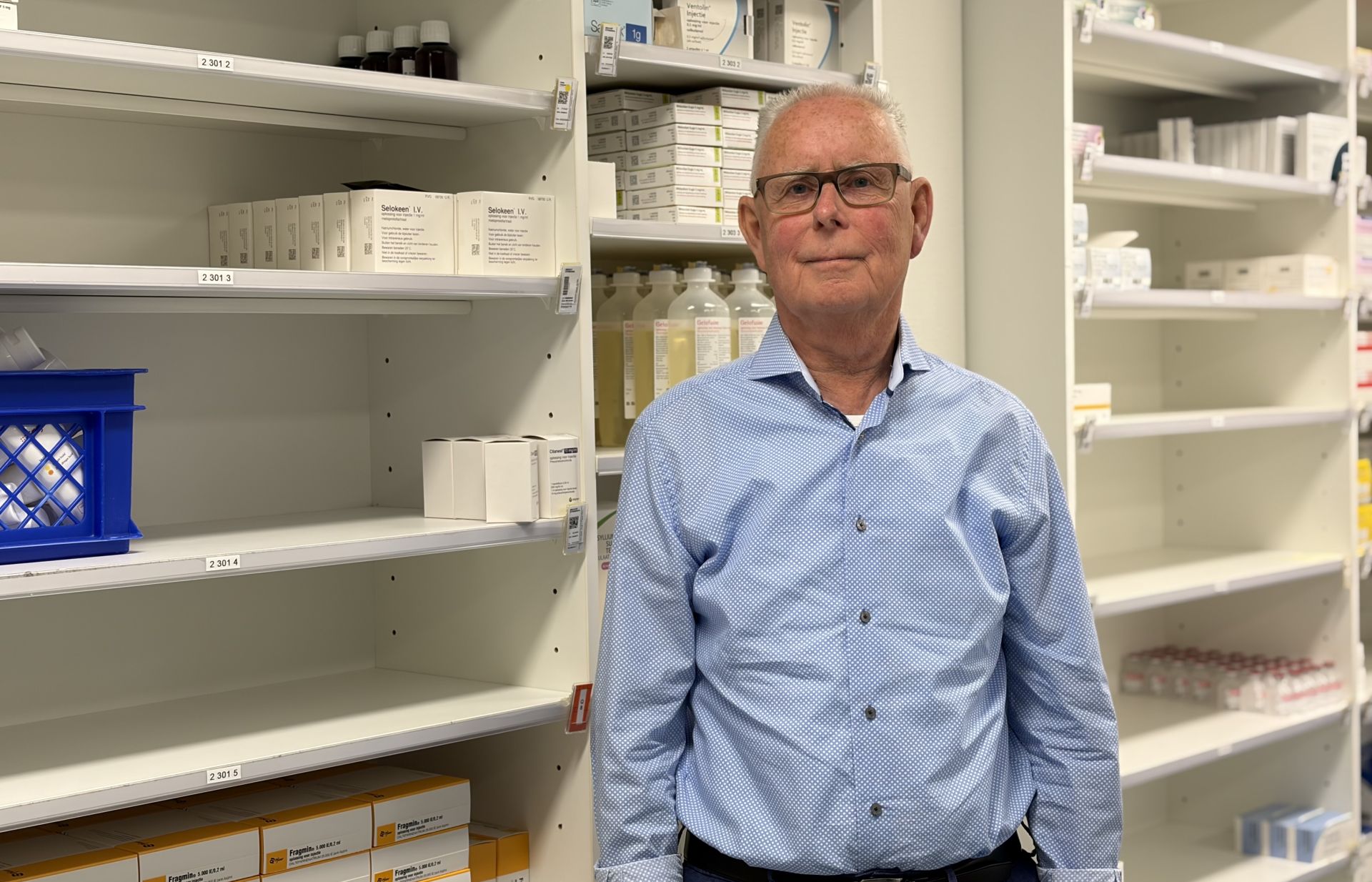 Een man in een apotheek met schappen vol medicijnen.